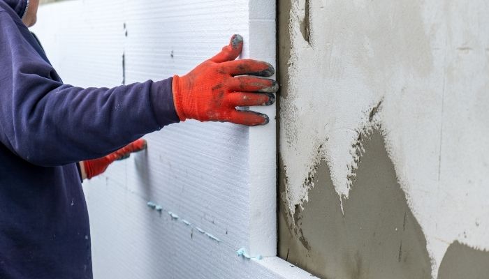 Pose d’un isolant thermique sur la façade d’une maison en brique par un ouvrier du bâtiment.